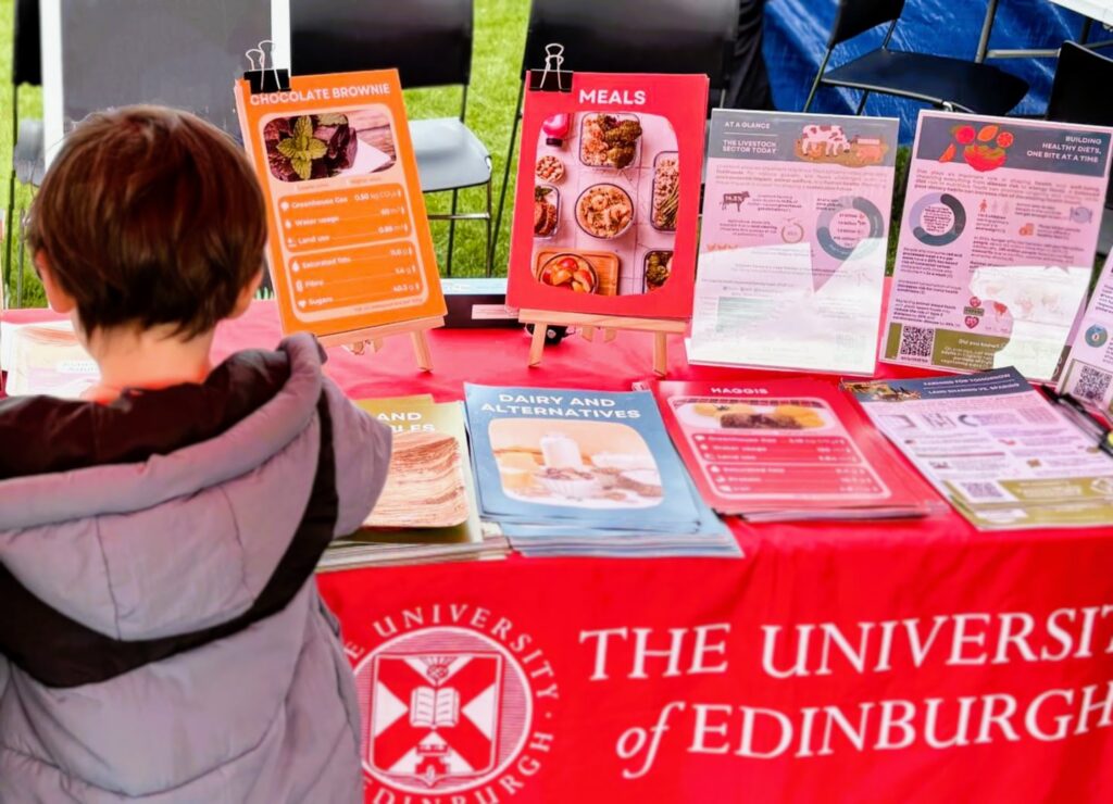 Person at a University of Edinburgh stall with top trumps-inspired food sustainability cards and infographics on display.