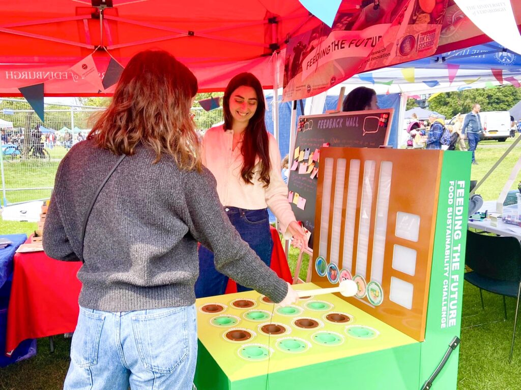 Two people at an outdoor event interacting with a Whac-a-mole-style food sustainability game.